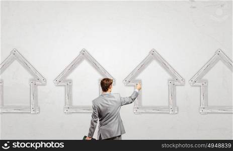 Real estate concept. Rear view of businessman fixing wooden house with hammer