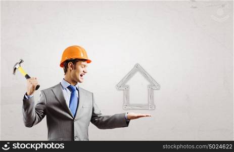 Real estate concept. Rear view of businessman fixing wooden house with hammer