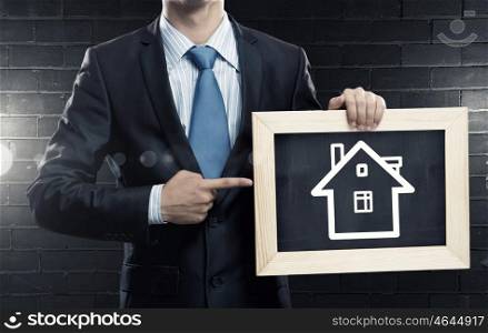 Real estate concept. Unrecognizable businessman holding wooden frame with house sketch