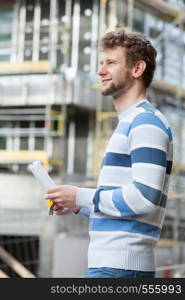 Real estate concept - young man on front of new big modern house building construction site with keys and blueprint project