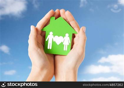 real estate, home and people concept - close up of hands holding green house with family pictogram