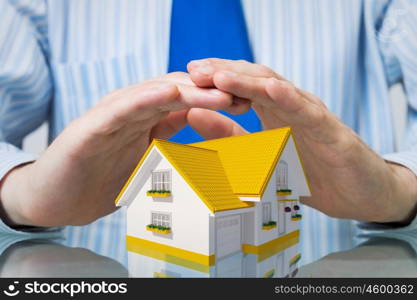 Real estate insurance. Hands of businessman covering house model with care