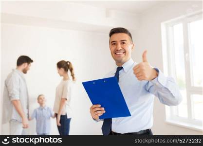 real estate, mortgage and people concept - happy smiling realtor with clipboard showing thumbs up and family at new home. realtor with clipboard showing thumbs up
