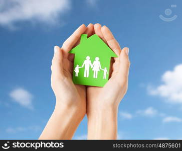 real estate, people and home concept - close up of female hands holding green paper house with family pictogram