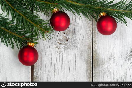 Real Grand Fir tree branch with three red ornaments on rustic white wooden boards. Christmas season concept.