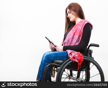 Real people, disability and handicap concept. Teen girl unrecognizable person sitting on wheelchair using tablet computer networking, studio shot on white