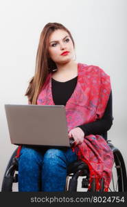 Real people, disability and handicap concept. Teen girl unrecognizable person sitting on wheelchair using laptop computer networking, studio shot on gray