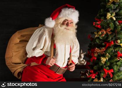Real Santa Claus carrying big bag full of gifts, at home near Christmas Tree