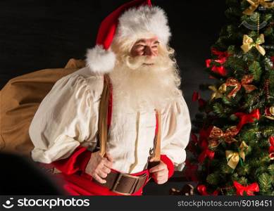 Real Santa Claus carrying big bag full of gifts, at home near Christmas Tree