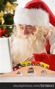 Real Santa Claus working on laptop with surprised face at home, surrounded by toys
