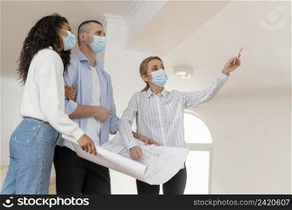 realtor couple with medical masks holding house plans