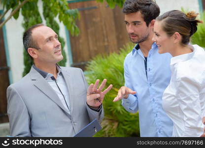 Realtor talking to young couple in front of property