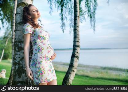 Realxed pregnant woman leaning against the tree