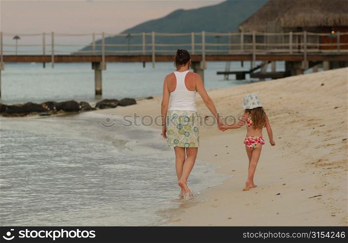 Rear of a young girl (6-8) walking with her mother on a beach, Moorea, Tahiti, French Polynesia, South Pacific