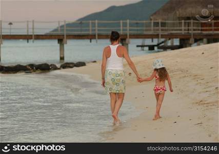 Rear of a young girl (6-8) walking with her mother on a beach, Moorea, Tahiti, French Polynesia, South Pacific
