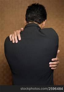 Rear profile of a young man hugging himself