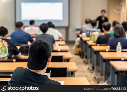 Rear side of Audiences sitting and listening the speackers on the stage in low light meeting room, event and seminar concept