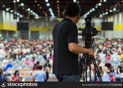 Rear side of Video Cameraman taking photograph to Abstract blurred photo of conference hall or seminar room in Exhibition Center background, event and seminar production equipment concept