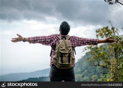 Rear view back of Young asian hiking man standing and rise-up hands with happy on peak of rocky mountain, copy space