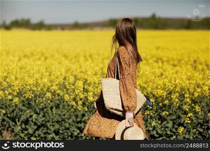 Rear view. beautiful young woman in a dress holding a hat and walking in a rapeseed field for summer, view from the back. copy space. summer holiday concept.. Rear view. beautiful young woman in a dress holding a hat and walking in a rapeseed field for summer, view from the back. copy space. summer holiday concept