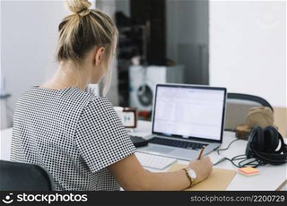 rear view businesswoman writing notes brown paper with laptop desk