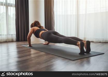 Rear view image of a young woman doing push up on training mat at home