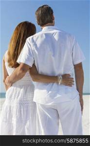 Rear view man and woman romantic couple embracing on a deserted tropical beach with bright clear blue sky