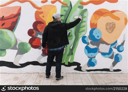 rear view man making graffiti with spray can wall