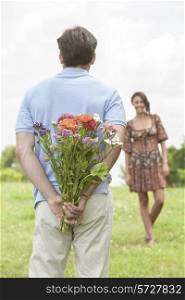 Rear view man surprising woman with bouquet in park