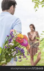 Rear view man surprising woman with bouquet in park