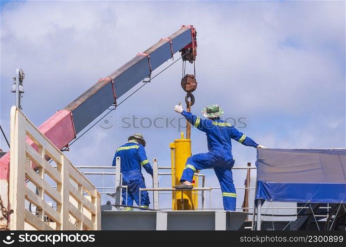 Rear view of 2 Asian engineer with crane truck are working to transferring yellow hydraulic cylinder into sand suction dredger ship at harbor