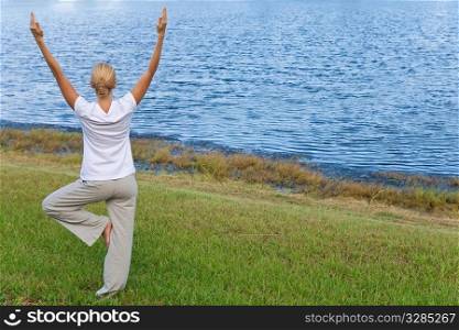 Rear view of a beautiful young blond woman practicing a yoga position by a tranquil blue lake