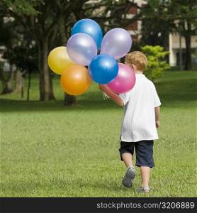 Rear view of a boy holding balloons in a park