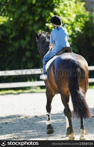 Rear view of a boy horseback riding