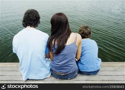 Rear view of a boy with his parents sitting on a pier