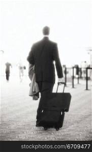 Rear view of a businessman in an airport pulling a suitcase
