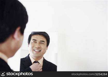 Rear view of a businessman looking into a mirror adjusting his tie