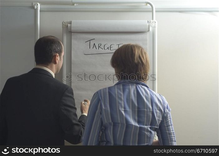 Rear view of a businessman with a businesswoman standing in front of a chart