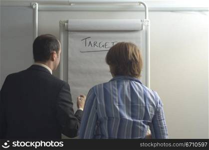 Rear view of a businessman with a businesswoman standing in front of a chart