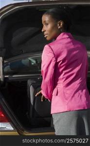 Rear view of a businesswoman loading her suitcase on a car trunk