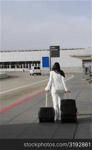 Rear view of a businesswoman pulling her luggage outside an airport