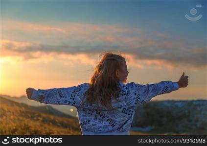 Rear view of a cheerful girl having fun in the mountains. Happy child with raised up hands enjoying mild sunset light. Active summer holidays.. People long for freedom and joy