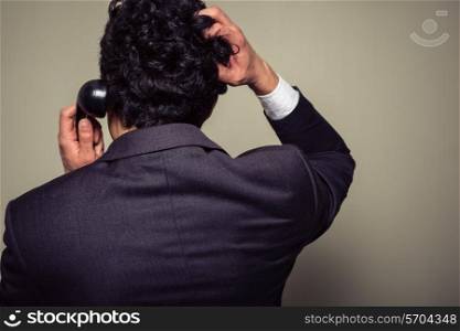 Rear view of a confused businessman on the phone scratching his head