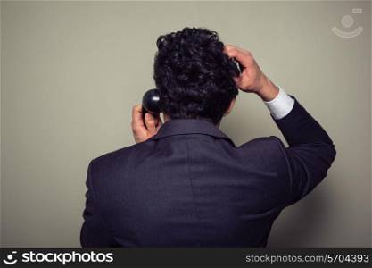 Rear view of a confused businessman on the phone scratching his head
