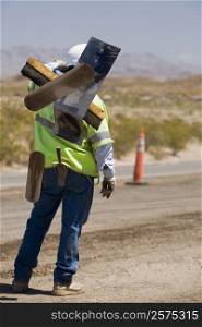 Rear view of a construction worker carrying hand tools on his shoulder