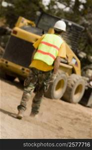 Rear view of a construction worker walking towards a bulldozer