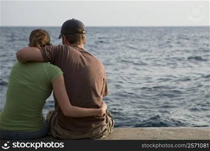 Rear view of a couple sitting at the seaside, Italian Riviera, Mar Ligure, Genoa, Liguria, Italy