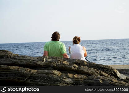 Rear view of a couple sitting at the seaside, Italian Riviera, Mar Ligure, Genoa, Liguria, Italy