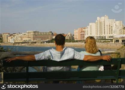 Rear view of a couple sitting on a bench, Grande Plage, Hotel du Palais, Biarritz, France