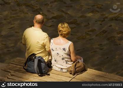Rear view of a couple sitting on a boardwalk, Bay of Naples, Sorrento, Sorrentine Peninsula, Naples Province, Campania, Italy